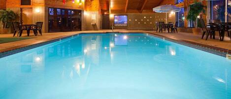 Una piscina interior con paredes y techo de madera, rodeada de mesas y sillas.