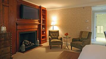 A hotel room with a fireplace, a television, two armchairs, a small table with a lamp, and a bed.
