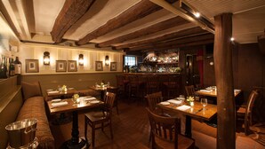 A restaurant with wooden beams, tables with white tablecloths, and a bar area.
