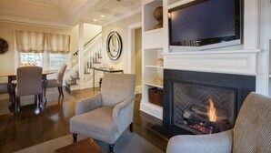 A living room with a fireplace, a television mounted above it, and a dining area in the background.