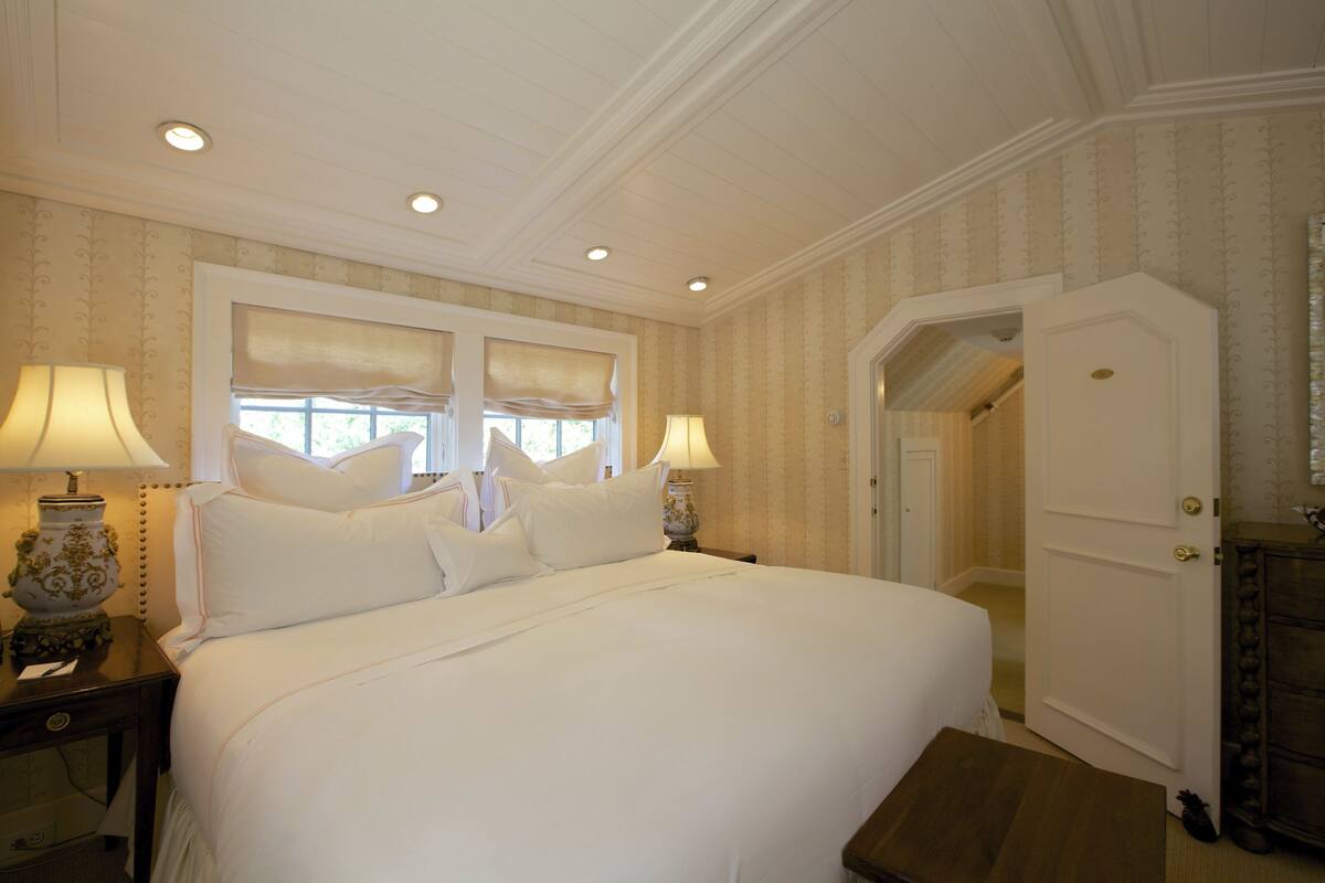 A neatly made bed with white linens, two bedside lamps, and a wooden nightstand.
