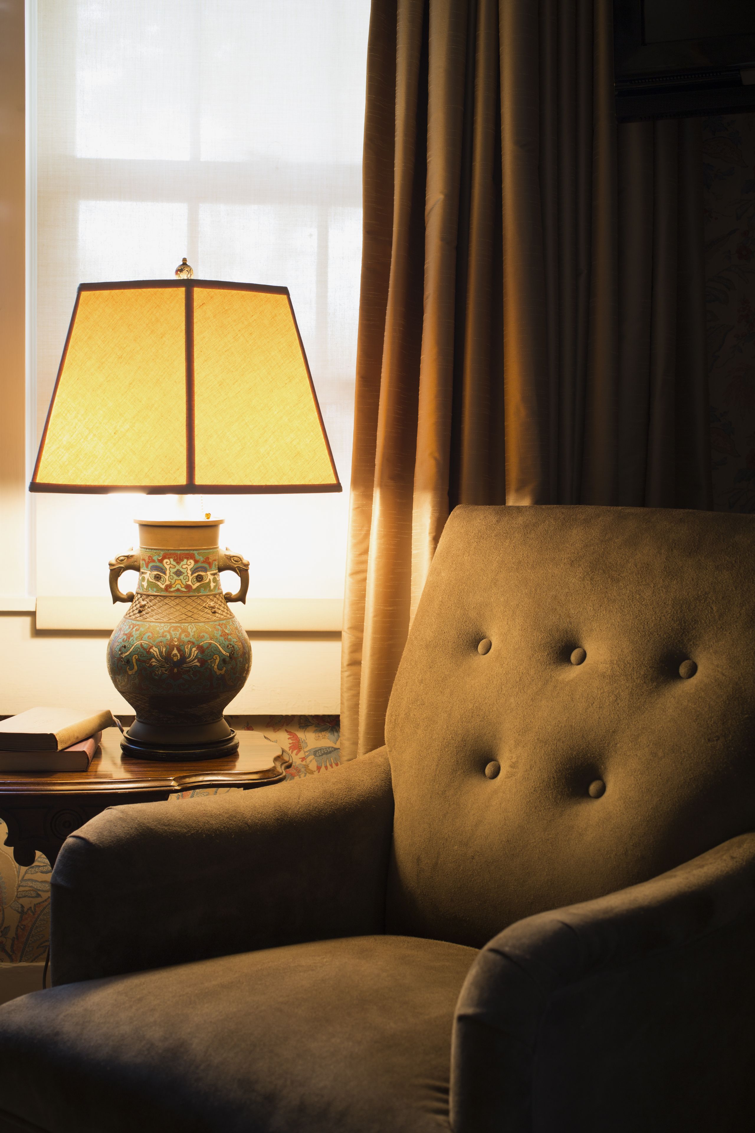 A chair with a cushion and a table with a lamp.