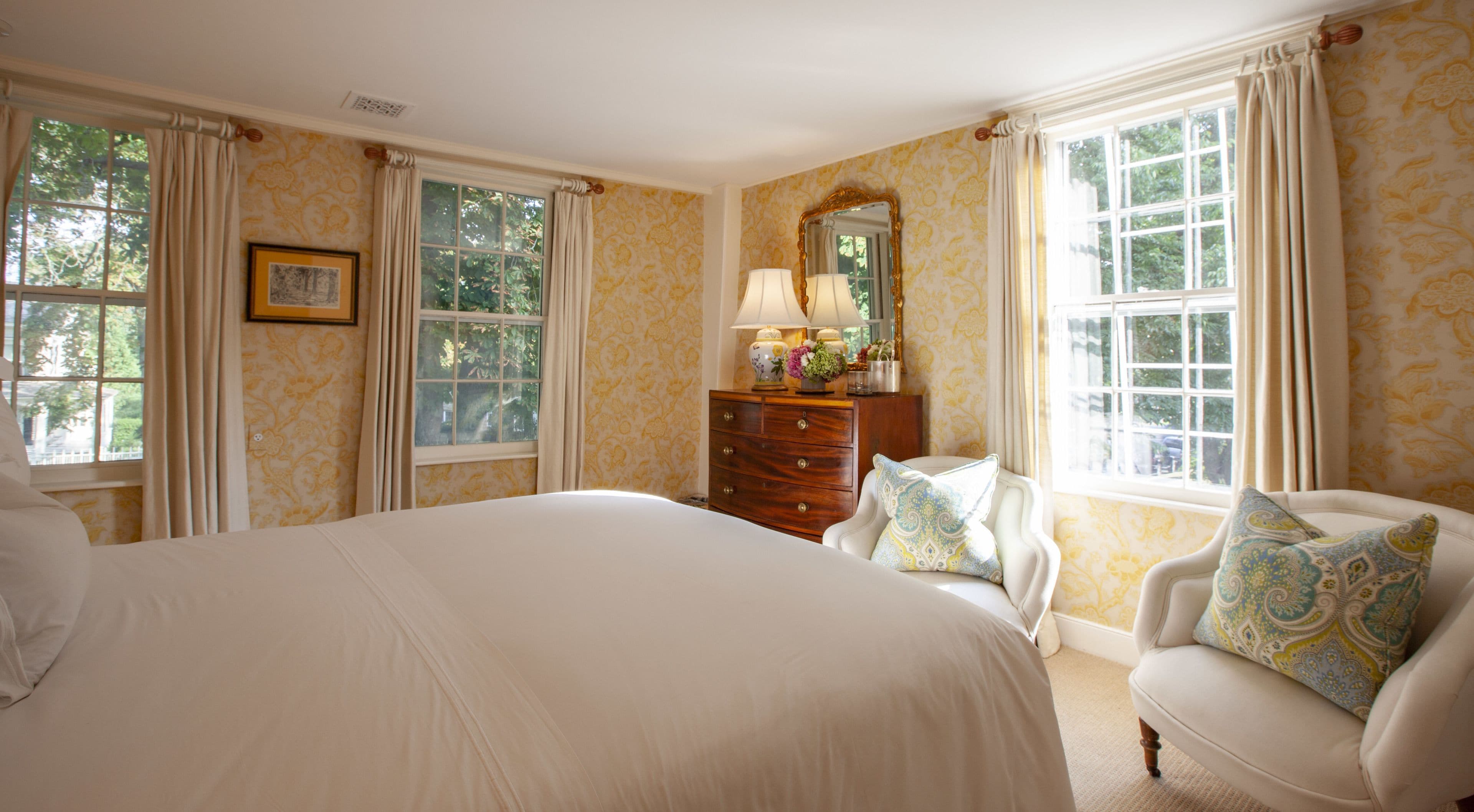 A bedroom with a large bed, a dresser, a chair, and a mirror.