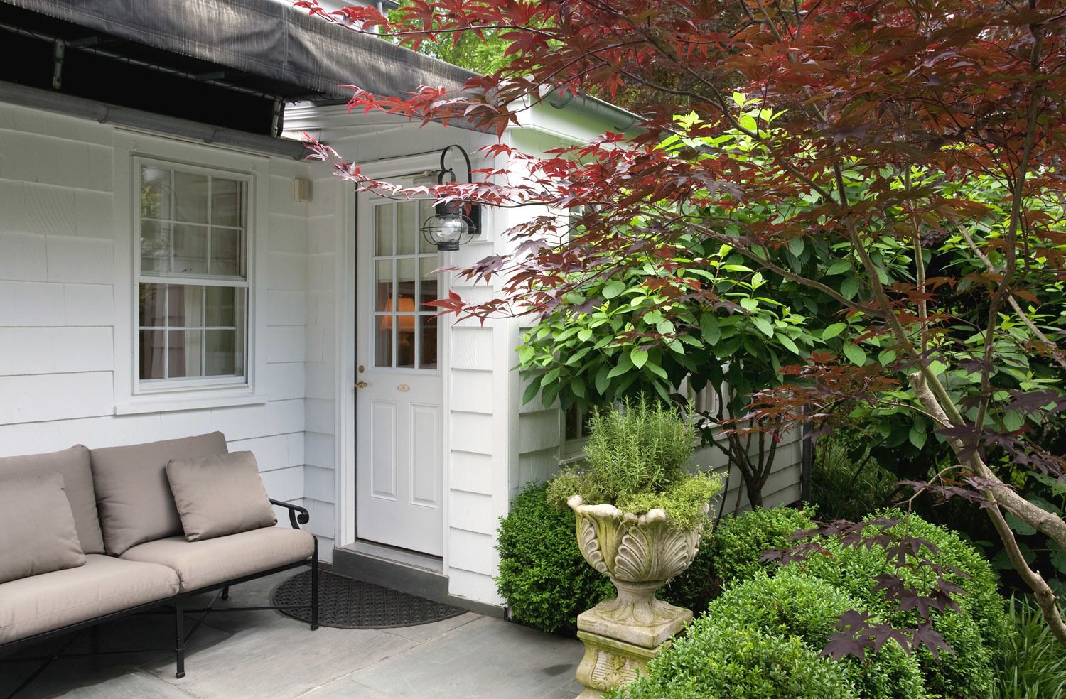 Une maison blanche avec un canapé beige et un bac à fleurs en pierre dans le jardin.