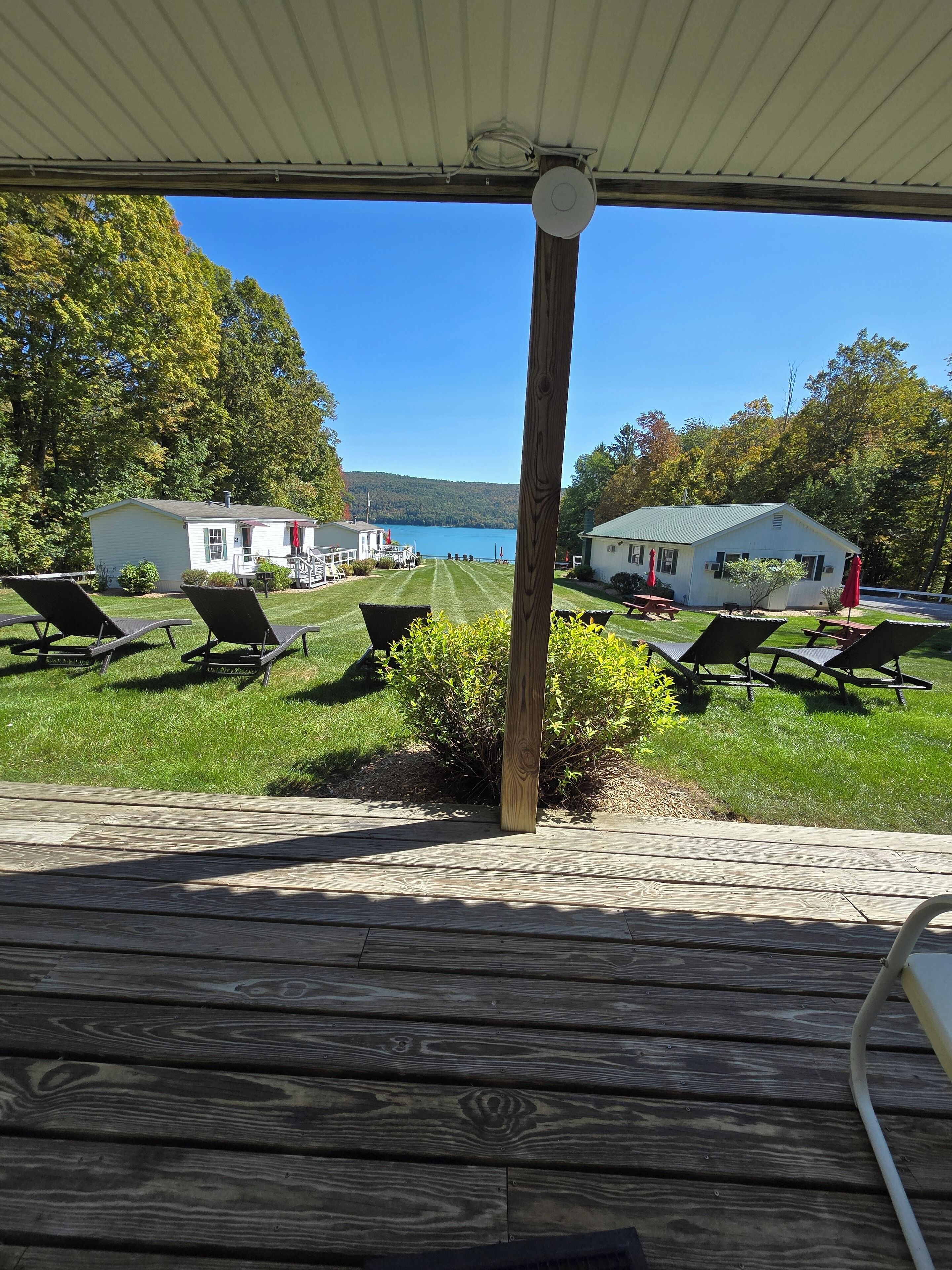 A wooden deck with lounge chairs overlooking a grassy area with small buildings and a lake.
