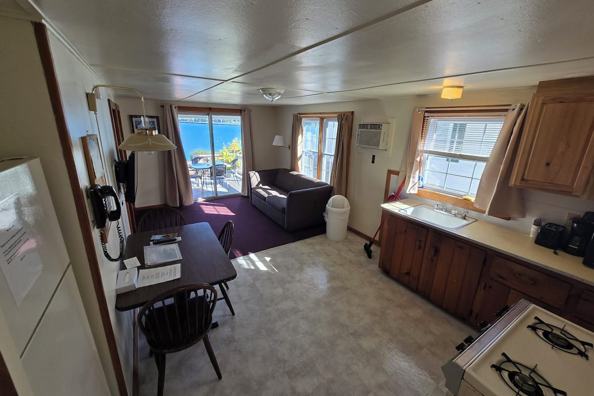 A compact hotel room with a kitchenette, a dining area, a sofa, and a view of the sea.