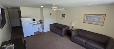 A compact living space with a kitchenette, two sofas, a small table, and a ceiling fan.