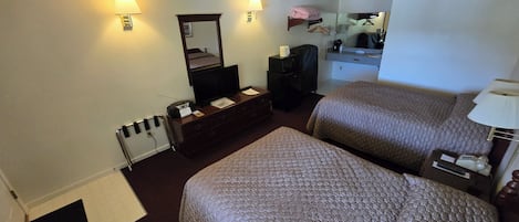 A hotel room with two beds, a TV, a dresser, a mirror, and a ceiling fan.