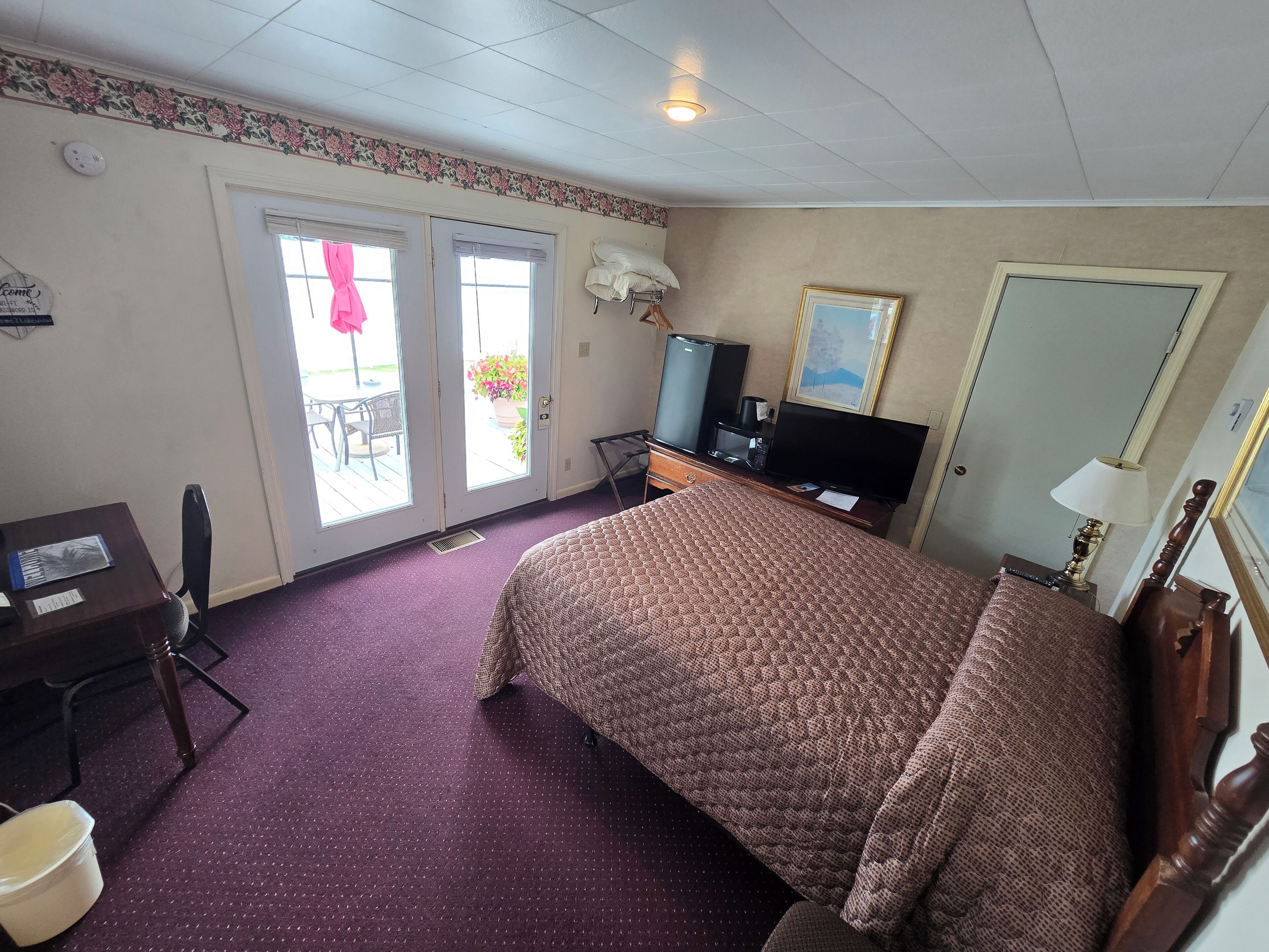 A hotel room with a bed, a desk, a chair, a television, and a window.