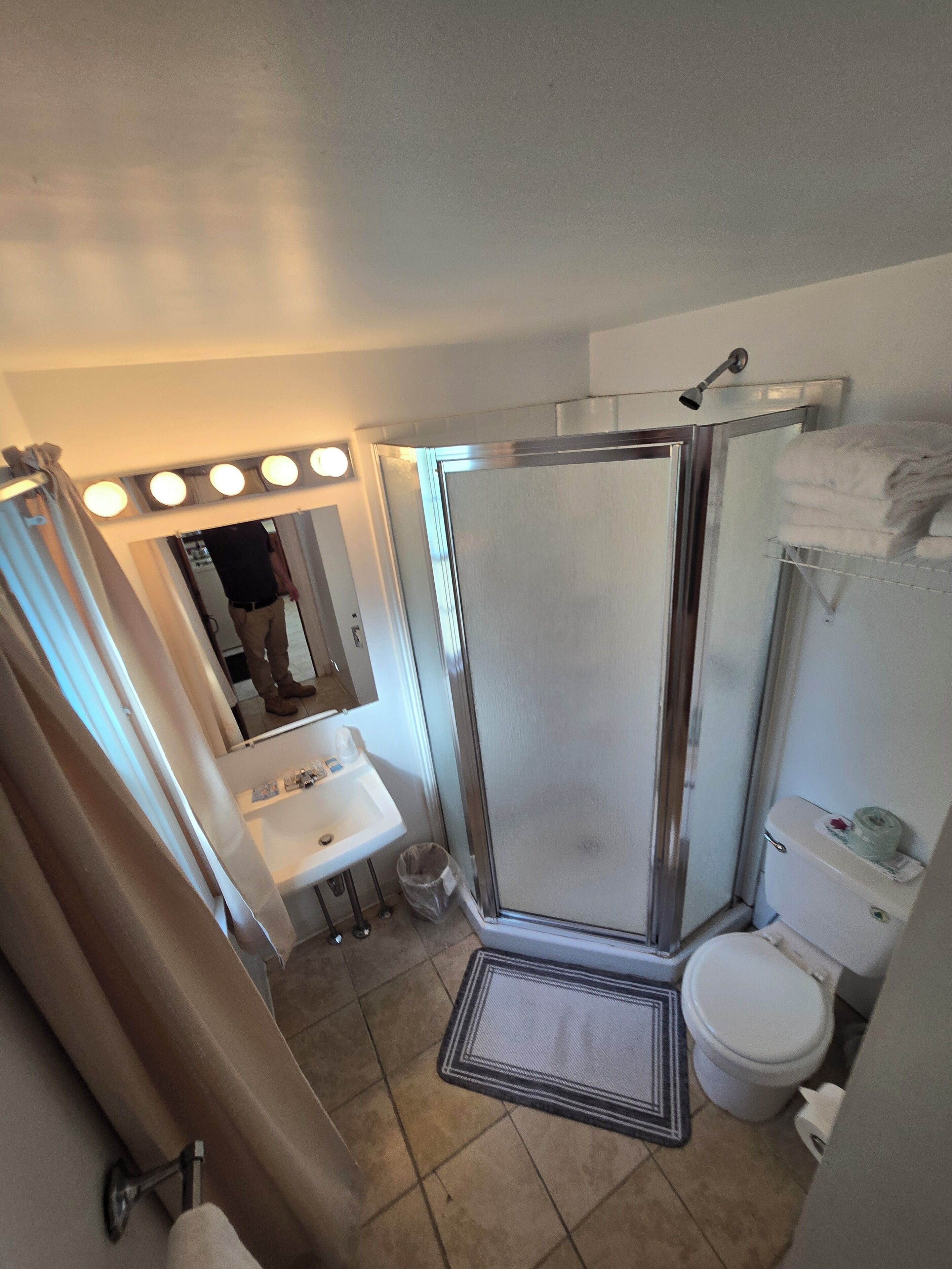 A bathroom with a shower, sink, and toilet. There are lights above the mirror and a towel rack.