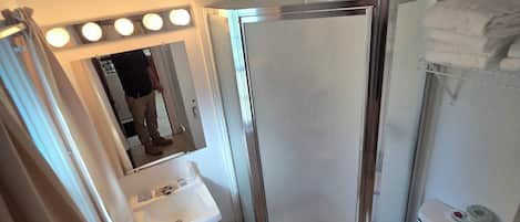 A bathroom with a shower, sink, and toilet. There are lights above the mirror and a towel rack.