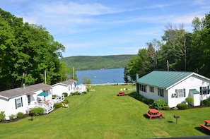 A lakeside cabin with a deck, picnic tables, and a well-maintained lawn. - Lake View Motel (Cooperstown)
