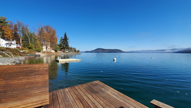 Un muelle de madera se extiende sobre un lago tranquilo de aguas azules cristalinas, rodeado de árboles y casas de colores otoñales.