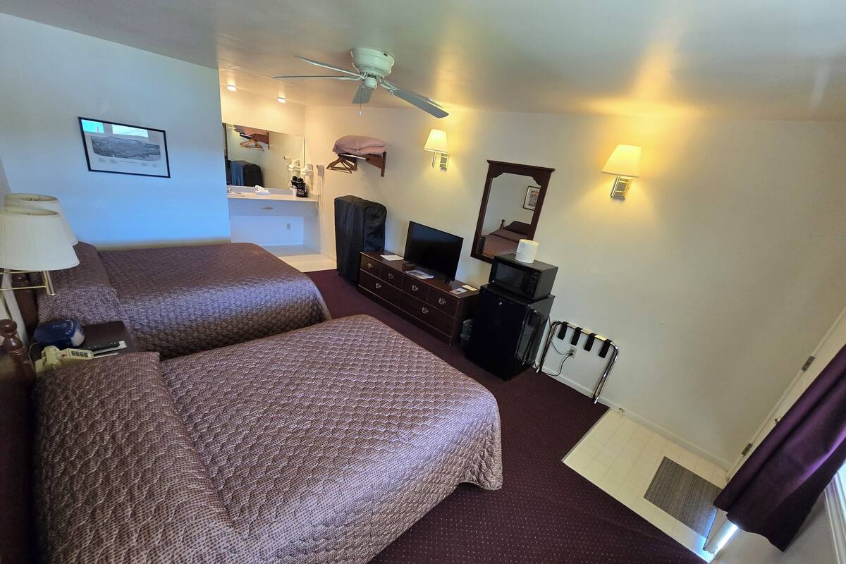 A hotel room with two beds, a desk with a computer, a microwave, a television, and a ceiling fan.
