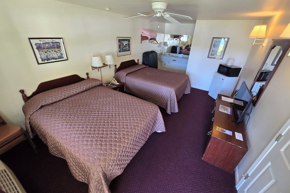 A hotel room with two beds, a desk with a computer, a microwave, and a ceiling fan.