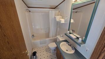 A bathroom with a bathtub, toilet, sink, and a mirror with lights.