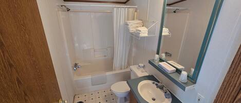 A bathroom with a bathtub, toilet, sink, and a mirror with lights.