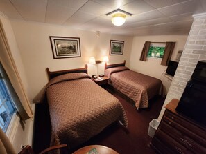 A hotel room with two beds, a desk with a lamp, a television, and framed pictures on the wall. - Lake View Motel (Cooperstown)