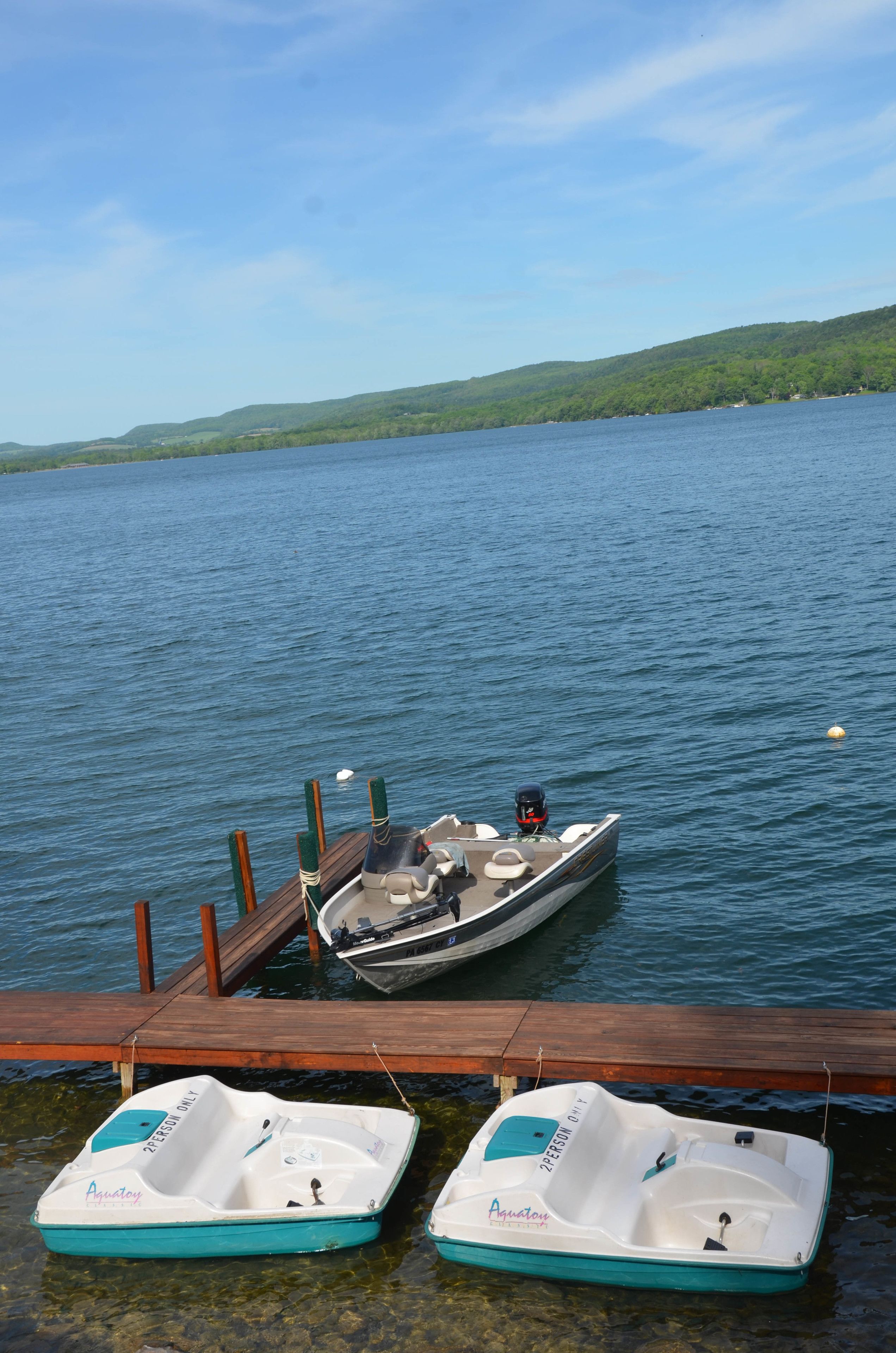 Two boats docked at a wooden pier with a lake and forested hills in the background.