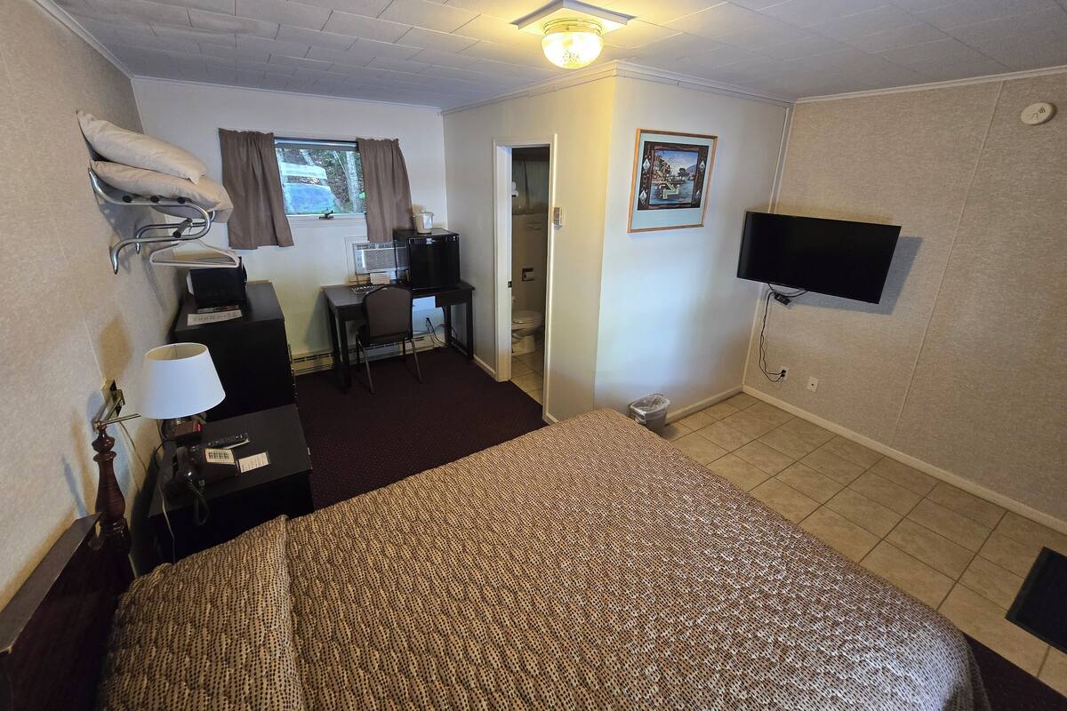 A hotel room with a bed, a desk with a computer, a TV, and a window with curtains.