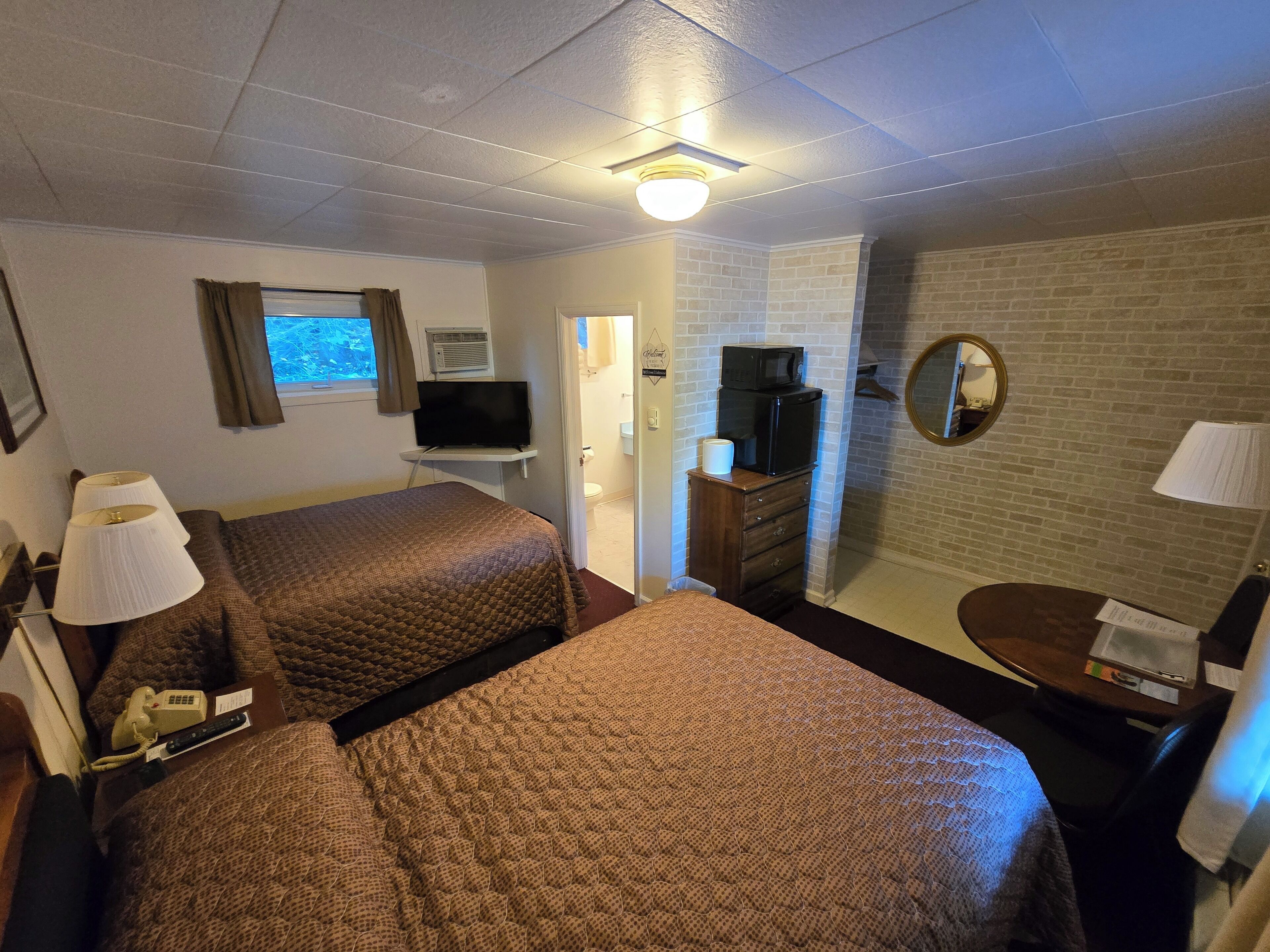 Habitación de hotel con dos camas, televisión, espejo, cómoda y ventana con cortinas.