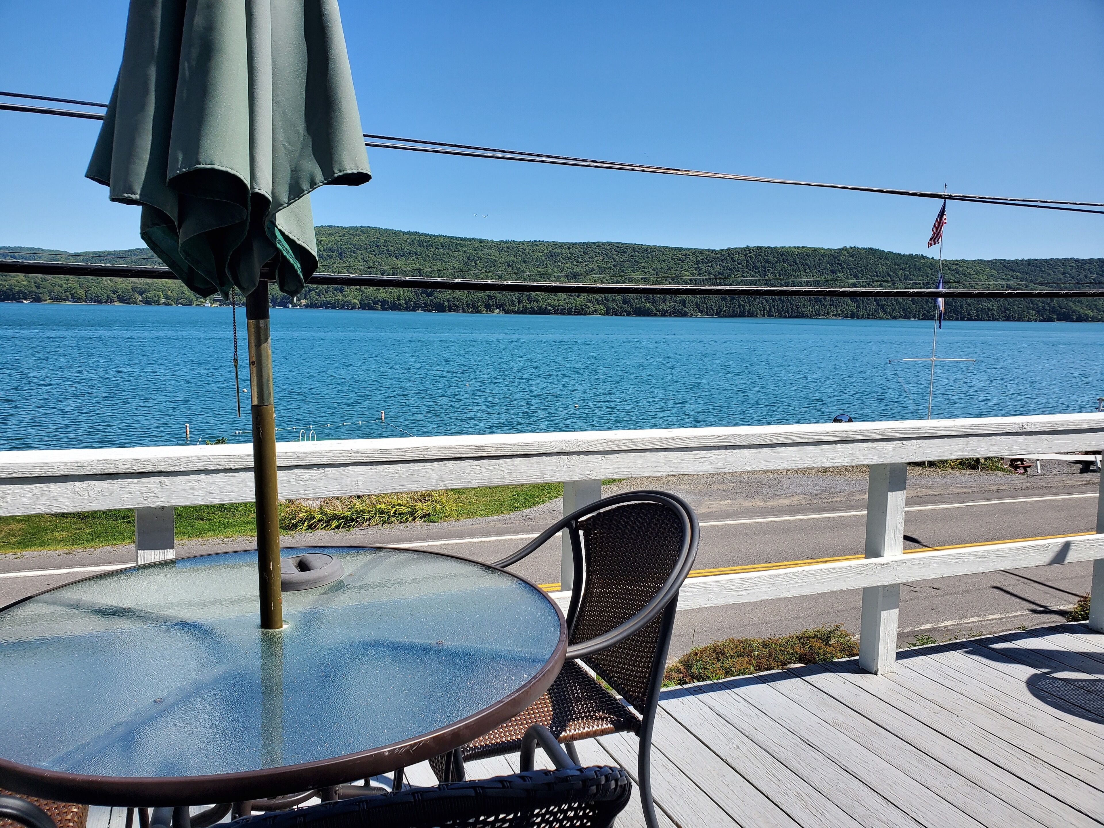 Une table avec un plateau en verre et une chaise en métal, donnant sur un lac avec une terrasse en bois et une rambarde.