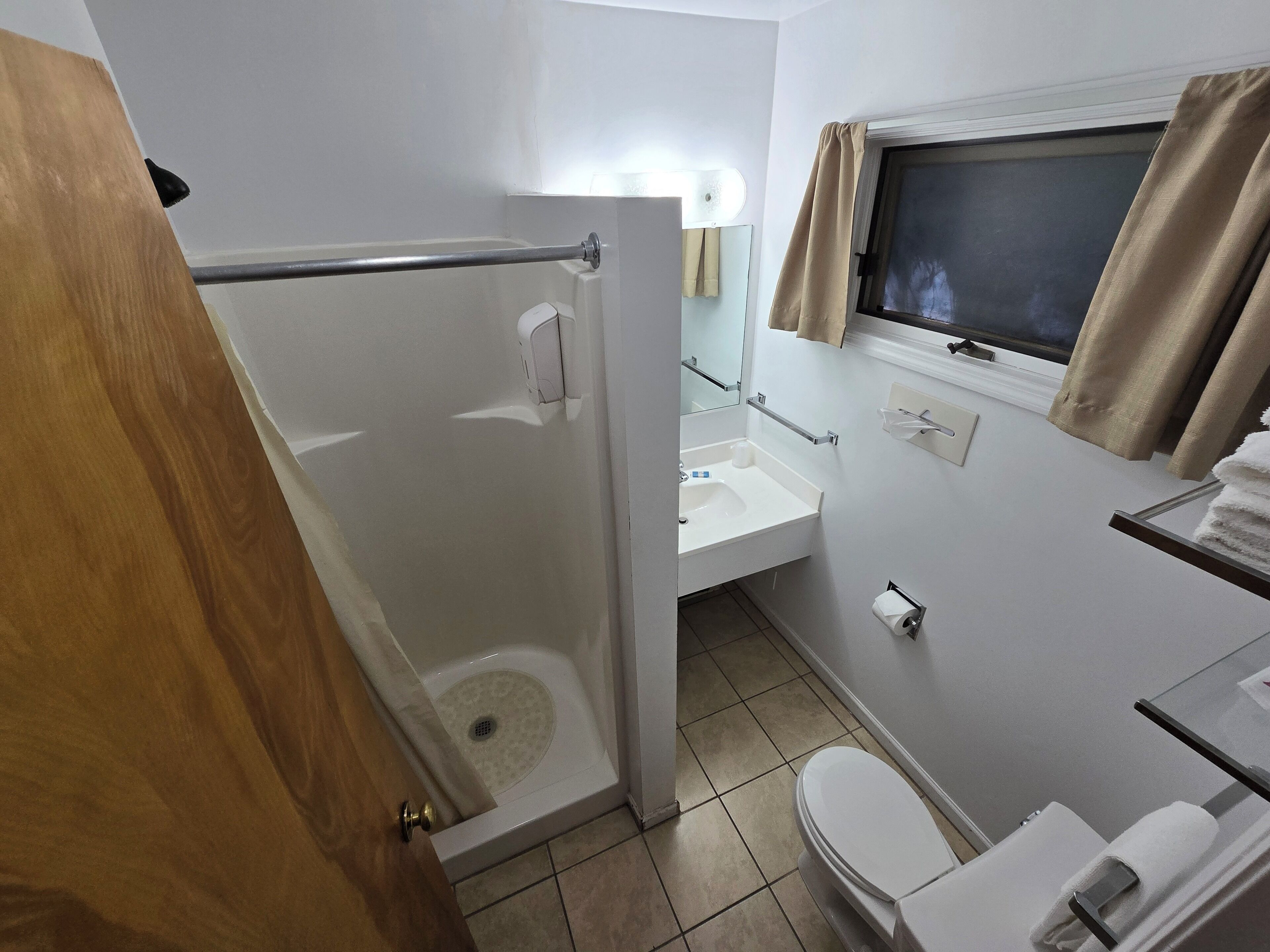 Een badkamer met douche, toilet, wastafel en een raam met gordijnen.