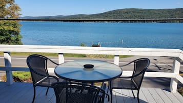 Una terraza con una mesa redonda y dos sillas, con vista a un lago que incluye un puente y colinas al fondo.