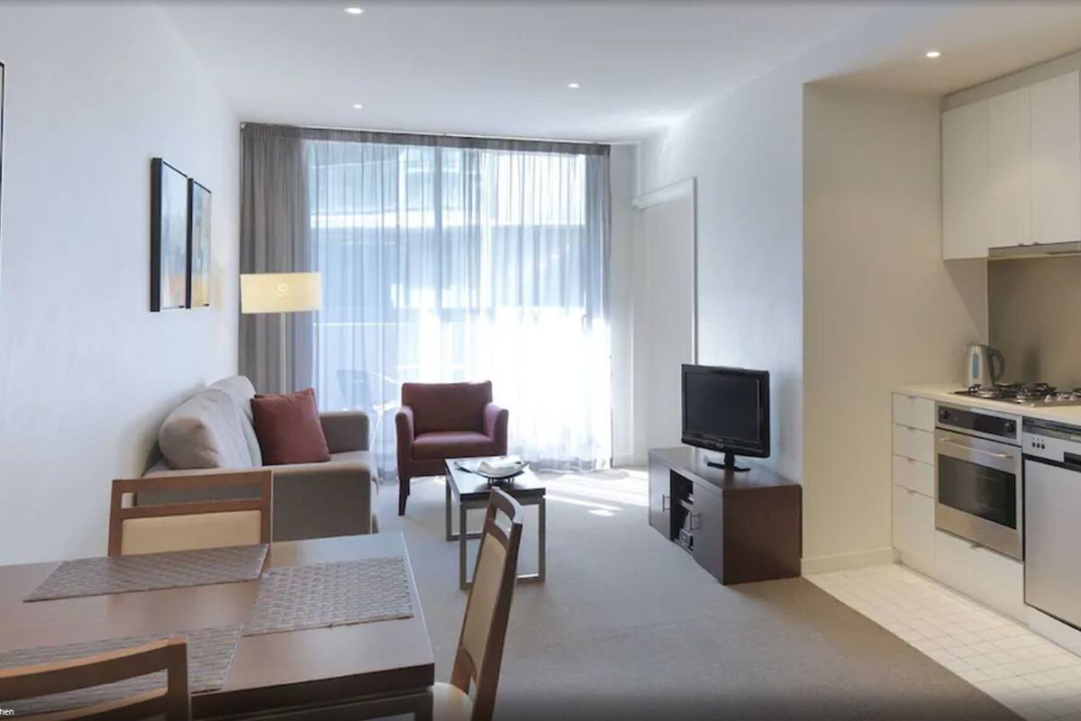 A modern kitchen with a dining area, a flat-screen TV, and a sofa.