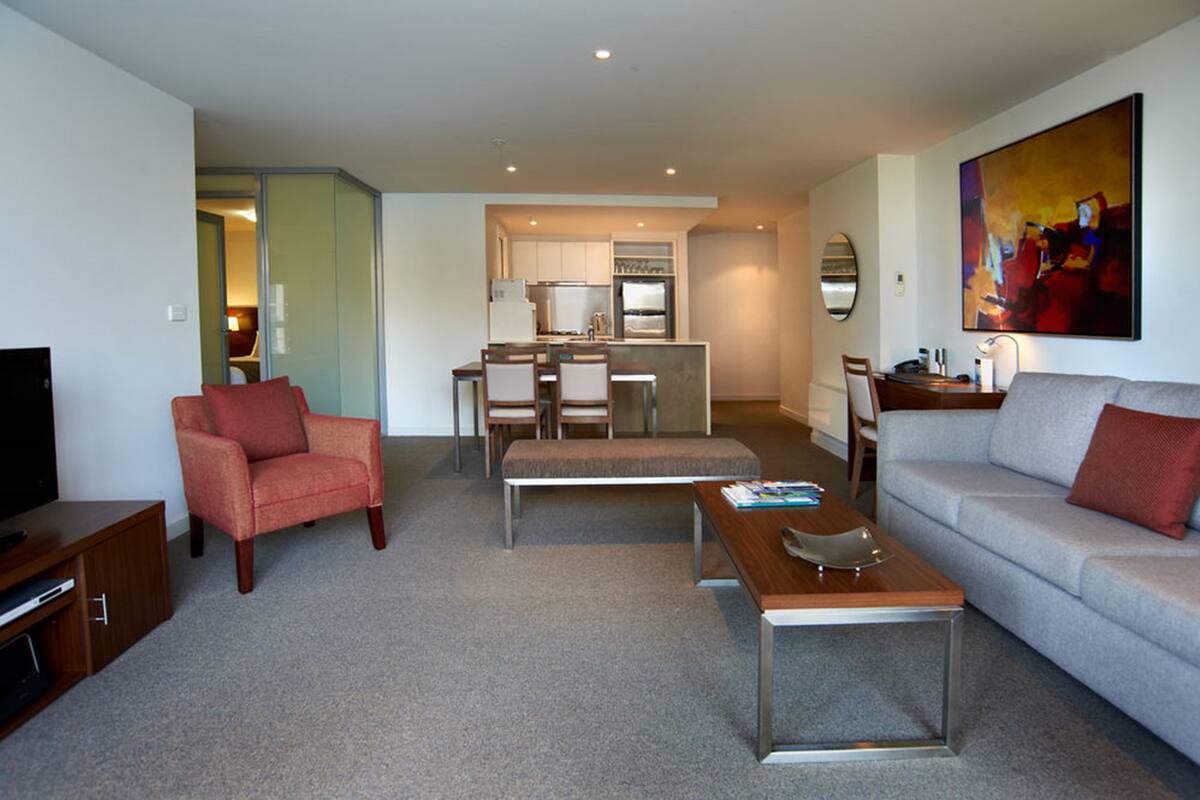 A modern living room with a sofa, armchair, coffee table, and a dining area with chairs and a table.