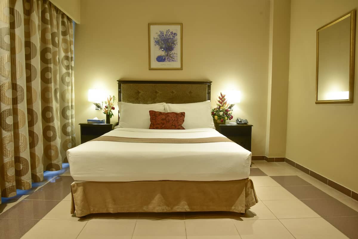 A hotel room with a large bed, two bedside tables with lamps, a framed picture on the wall, and a mirror on the wall.