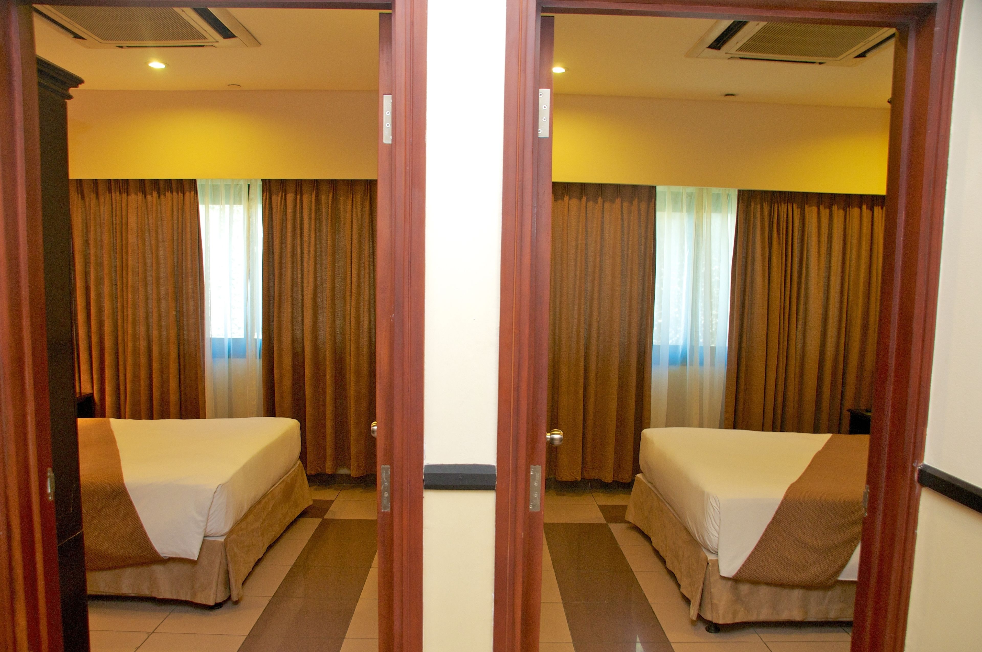 A hotel room with two beds, a large window with curtains, and a door with a mirror.