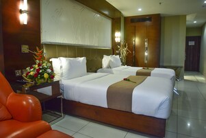 A hotel room with two beds, a wooden headboard, a nightstand with a vase of flowers, and a red leather chair.