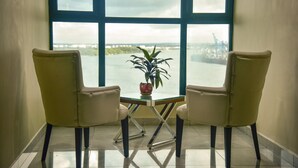 Habitación con dos sillas mirando hacia una ventana con vista al agua y un paisaje urbano distante.