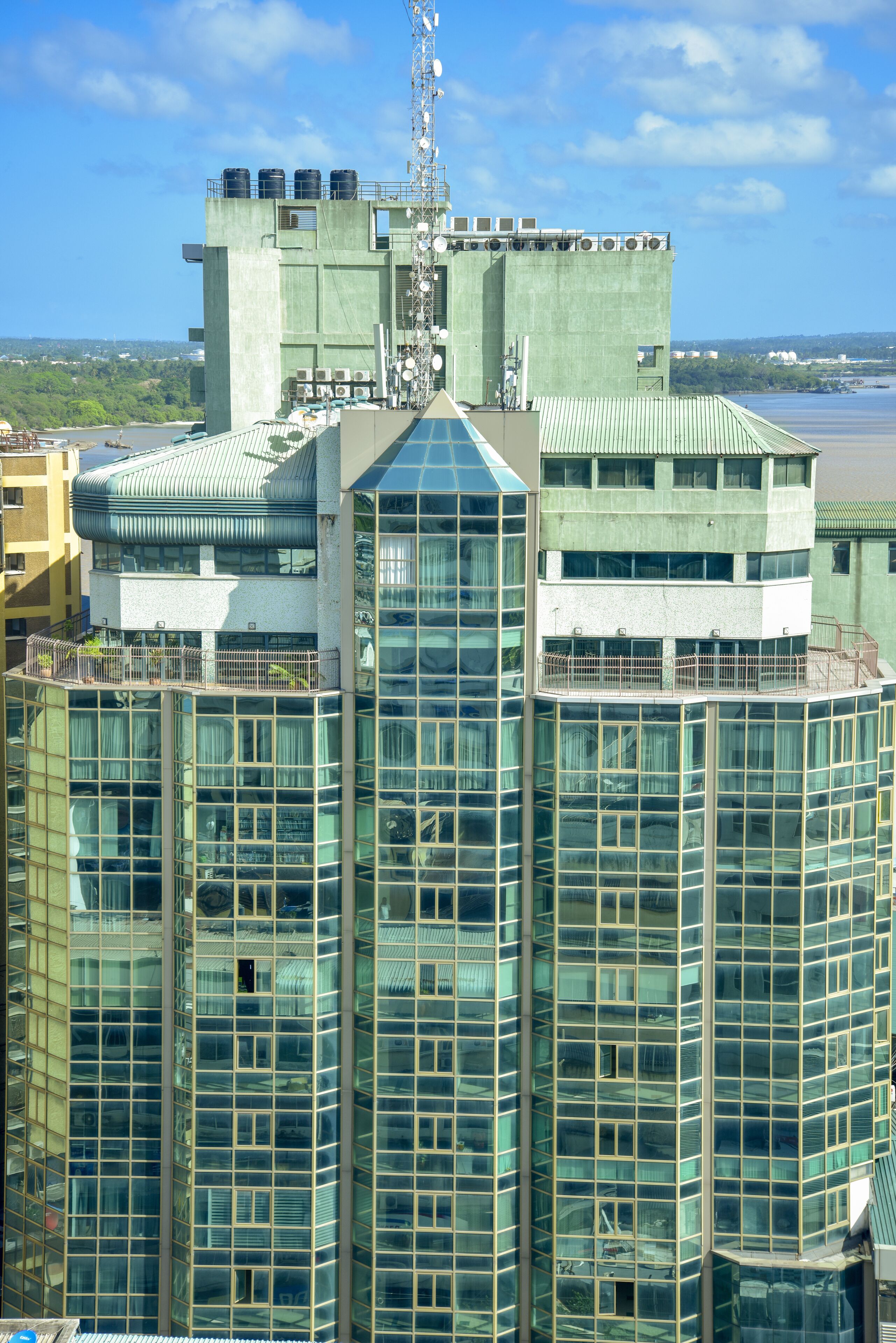 Un edificio moderno de gran altura con fachada de vidrio, varios balcones y una azotea con tanques de agua.