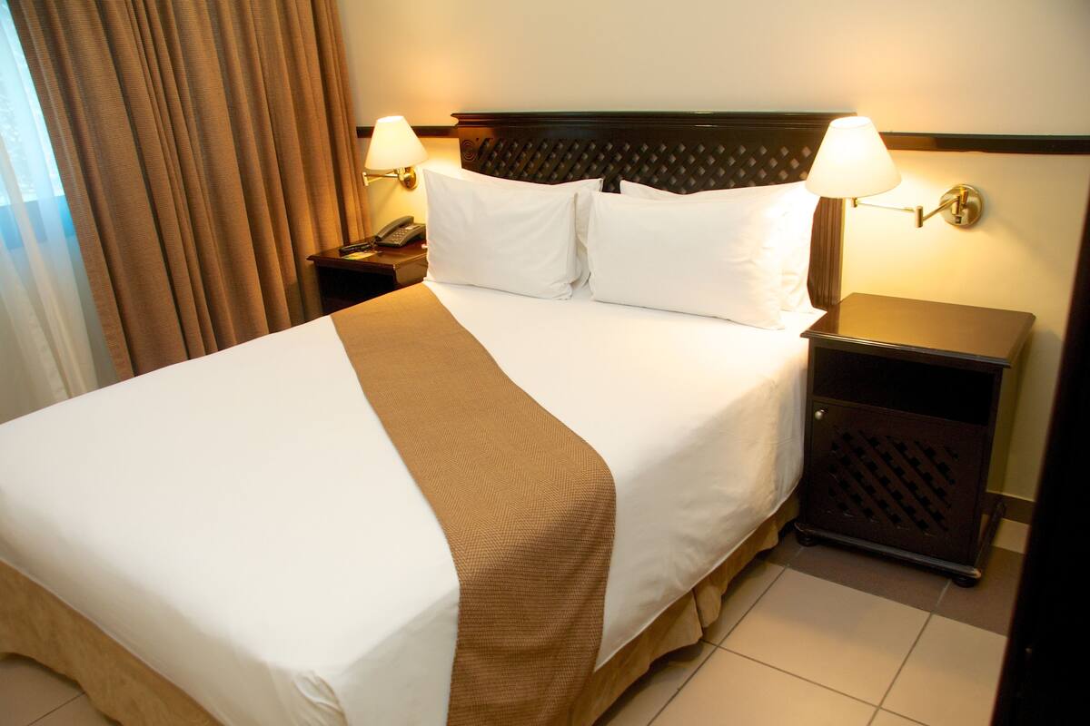 A hotel room with a large bed, two bedside lamps, a telephone, and a small cabinet.
