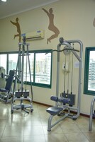 Un gimnasio con equipo de ejercicio, ventanas amplias y vistas a edificios.