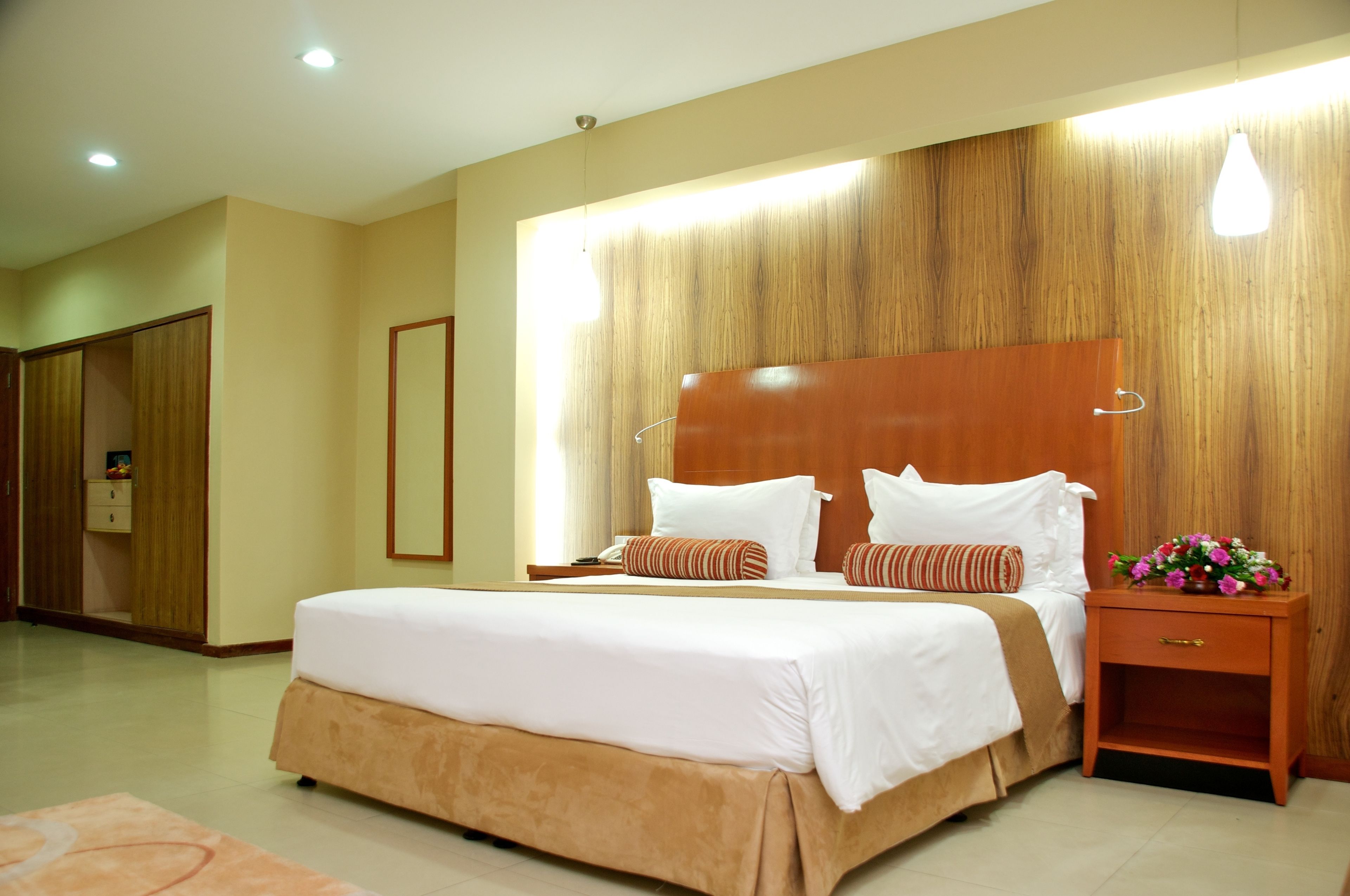 A hotel room with a large bed, wooden headboard, bedside tables, and a nightstand with a vase of flowers.