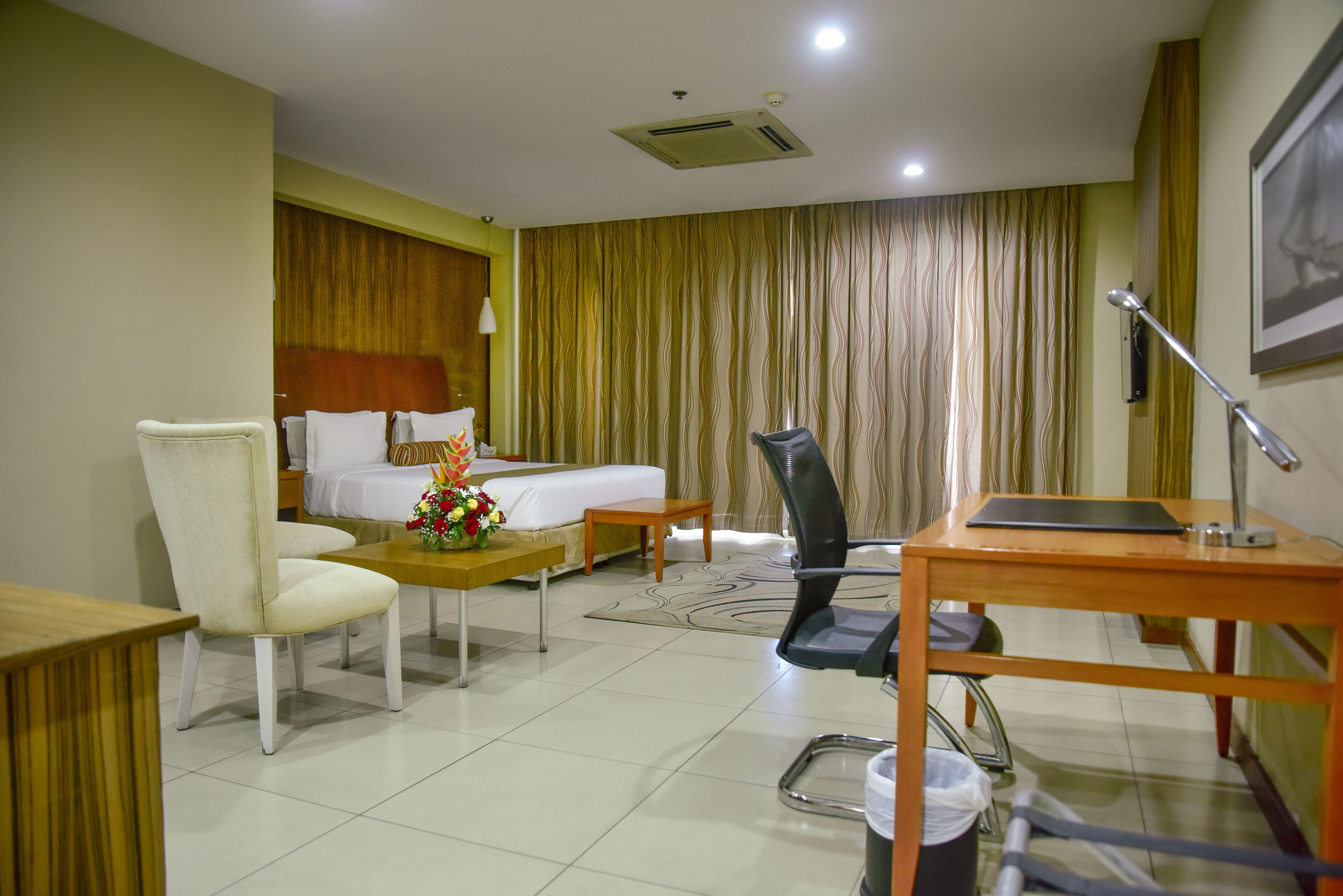 Una habitación de hotel con cama, escritorio, silla, mesita y cubo de basura.