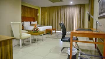 Una habitación de hotel con cama, escritorio, silla, mesita y cubo de basura.