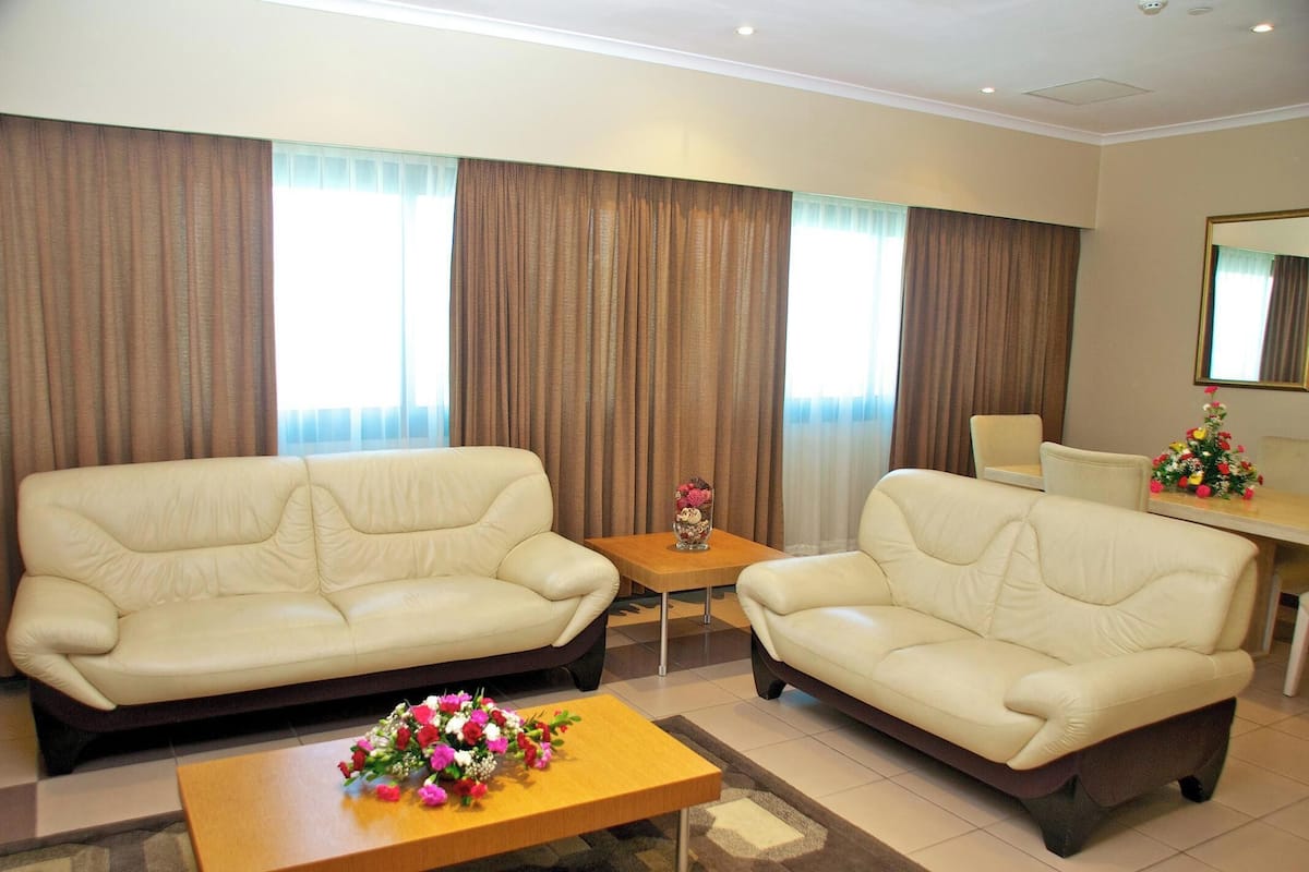 A hotel room with two sofas, a small table with a vase, and a dining area with a chair and table.