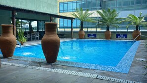 Una piscina con un letrero que dice 'NO DIVING', rodeada de macetas de terracota grandes y palmeras, con un edificio moderno al fondo.