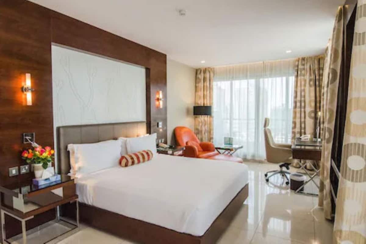 A modern hotel room with a large bed, a desk, a chair, and a TV.