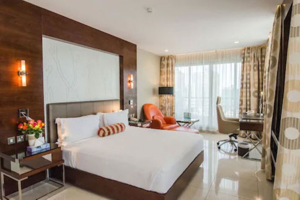 A hotel room with a large bed, a desk, a chair, and a TV.