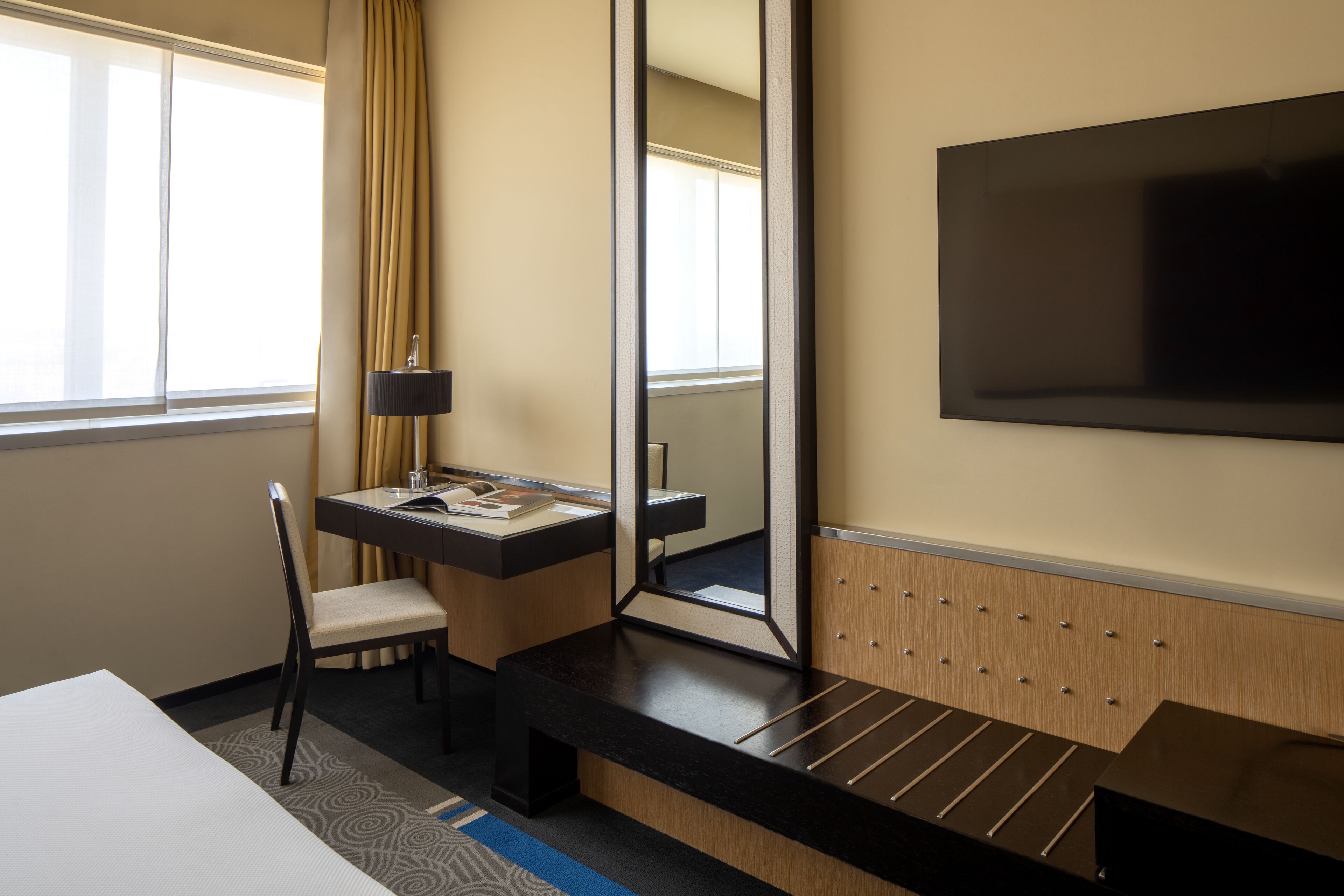 Ein Hotelzimmer mit einem Bett, einem Schreibtisch, einem Sessel, einem Fernseher und einem großen Spiegel.