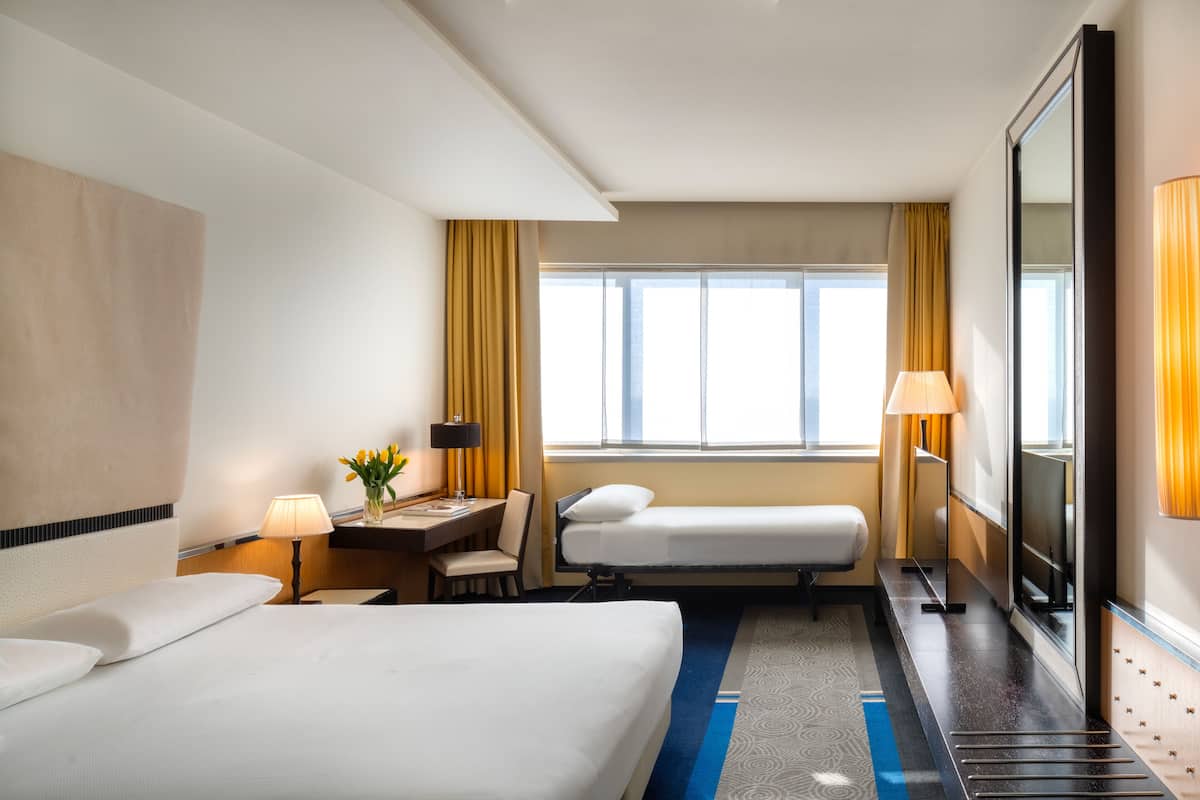 Habitación de hotel con dos camas, un escritorio con lámpara, televisión y un espejo grande.