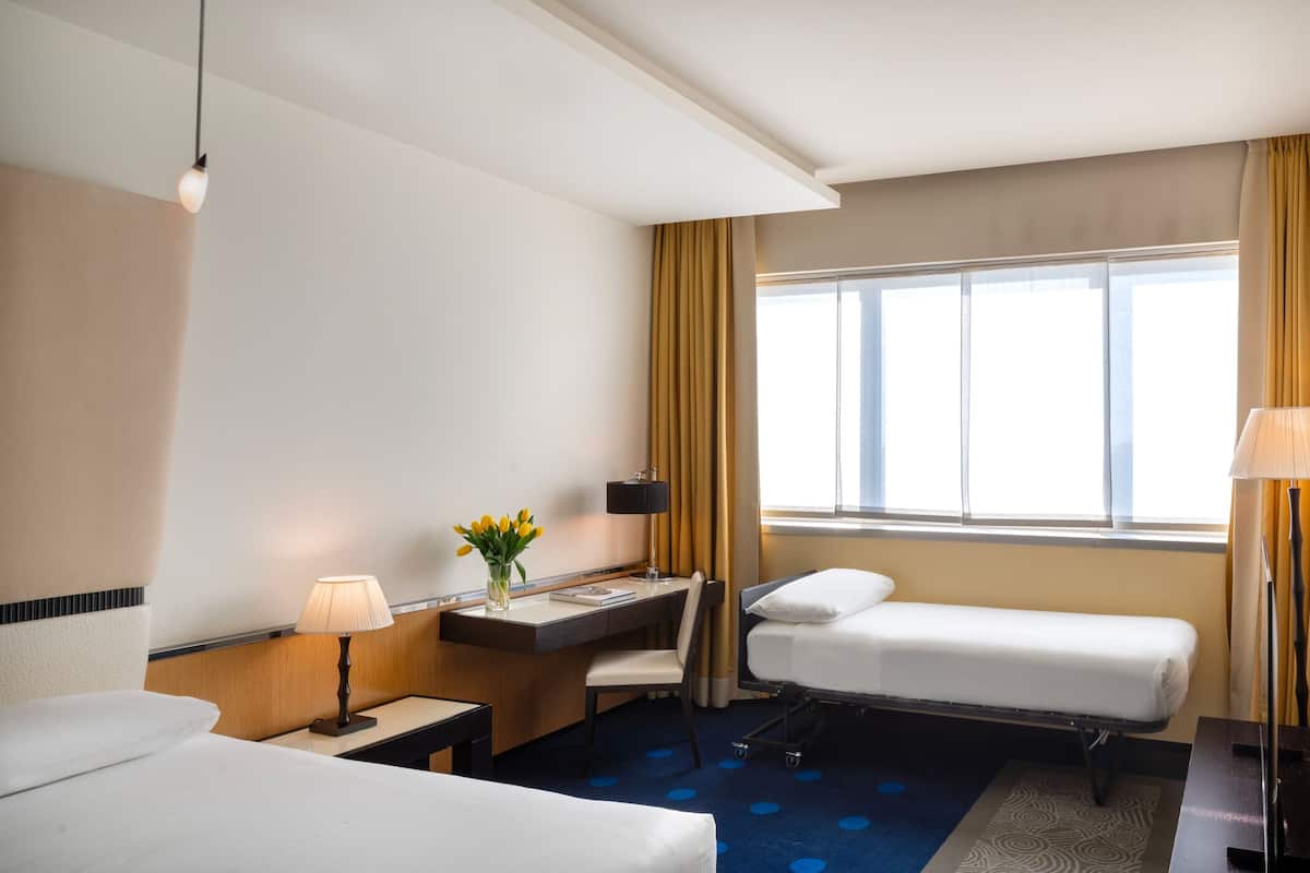 Habitación de hotel con cama, escritorio con lámpara, silla y ventana con cortinas.