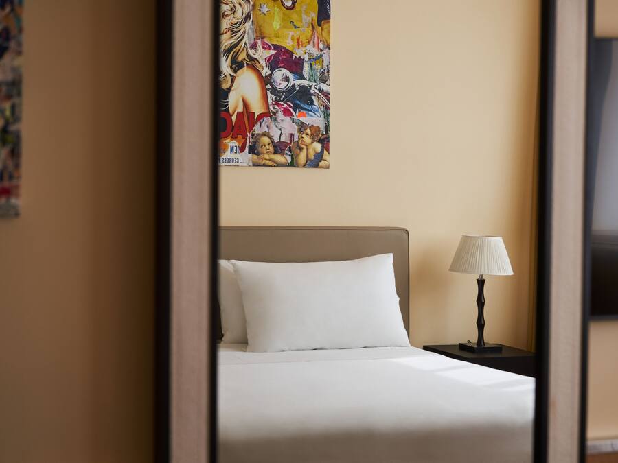 A hotel room with a bed, a nightstand with a lamp, and a colorful abstract painting on the wall.
