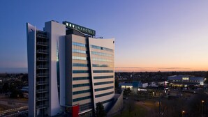 A modern hotel with a prominent 'UNAHOTELS' sign, a large parking area, and a Burger King across the street. - UNA Hotels Malpensa (Cerro Maggiore)