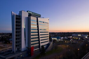 A modern hotel with a prominent 'UNAHOTELS' sign, a large parking area, and a Burger King across the street.